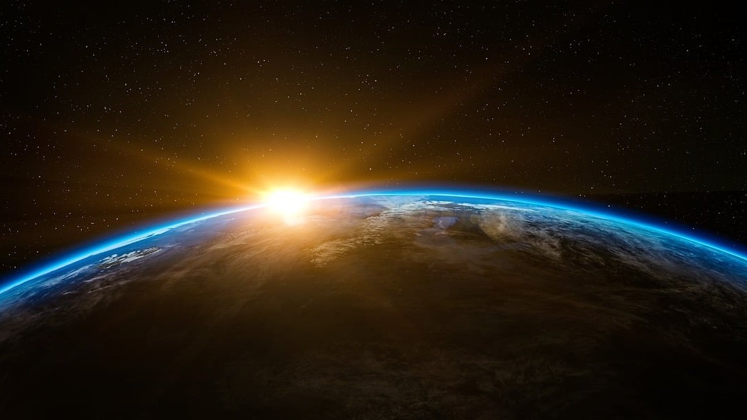 Photo of Earth and space with sun peeking over the planet's horizon. 