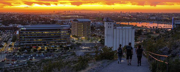 Photo of three students hiking down A Mountain in Tempe at sunset with downtown Tempe in the background 