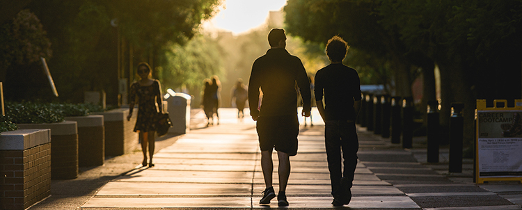 Image of two students walking outside in silhouette. 