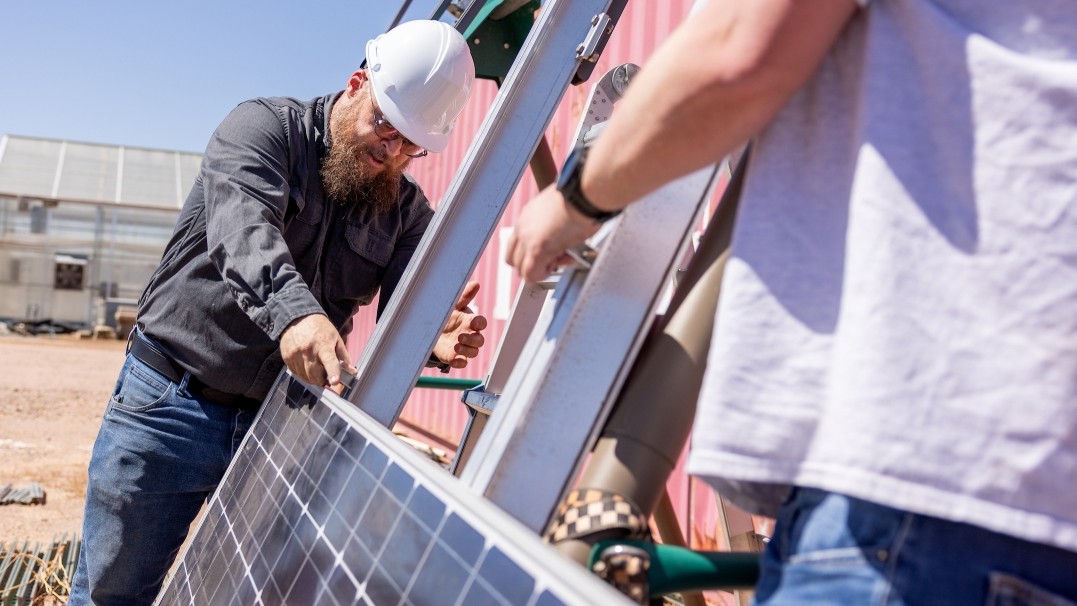 The upcoming American Association for the Advancement of Science Annual Meeting will feature ASU experts from a range of fields, including engineer Alexander Mobley (pictured) in a hard hat and working with a solar panel with another person whose back is to the camera. Mobley will co-lead a workshop on microgrids. 