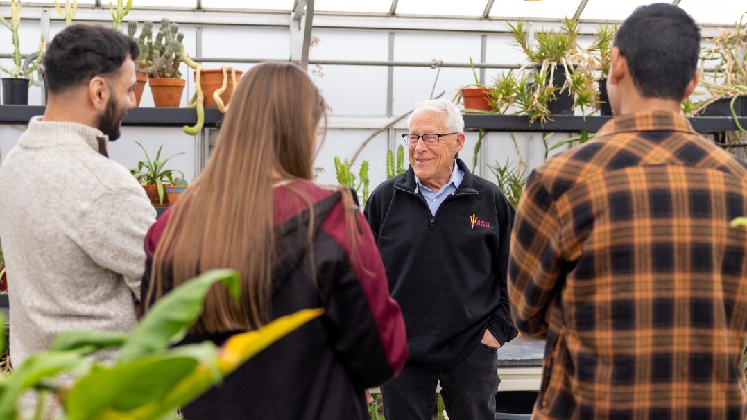 Image of Rob Walton in ASU jacket talking to two male and one female students in a greenhouse on campus. 
