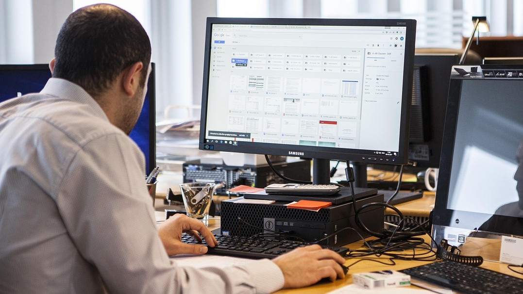 Image of a man working on a computer with another computer screen to his right. 