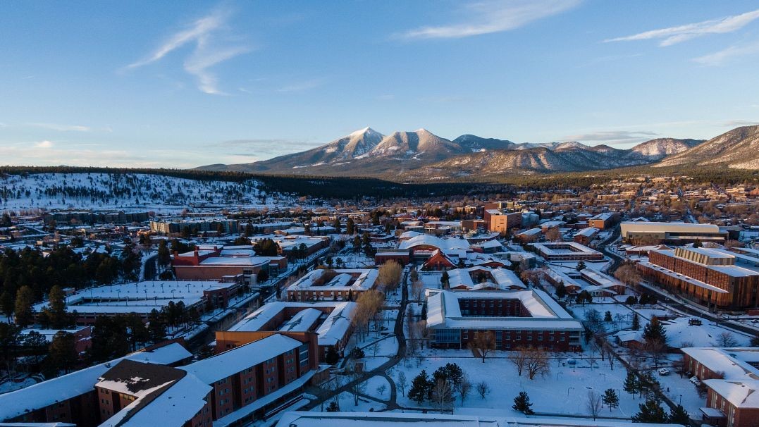 Aerial image of the NAU Flagstaff campus covered in snow with the San Francisco Peaks in the background 