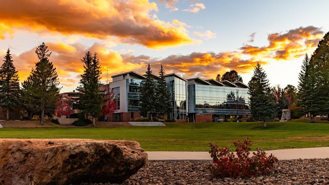 A building on NAU's campus with a beautiful sunset in the background and pine trees in the image. 