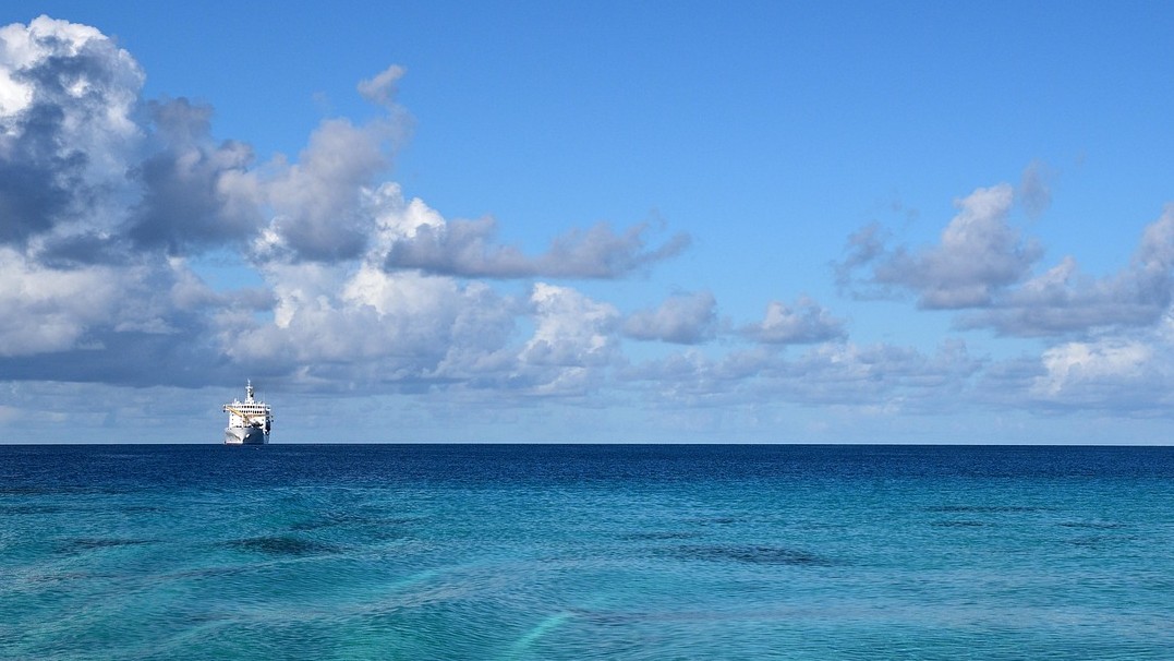 Image of a ship at sea with puffy clouds in the sky 