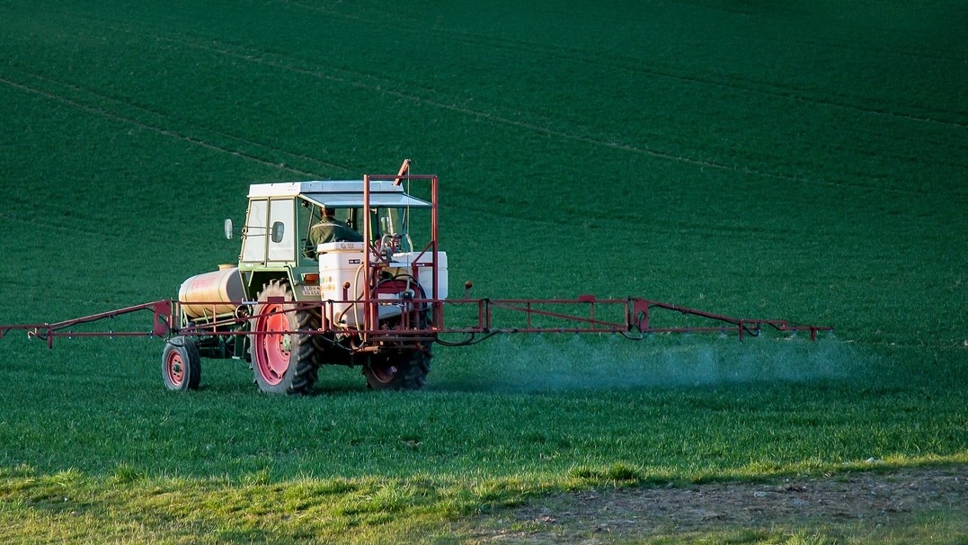 A tractor spreads pesticides on a field. 