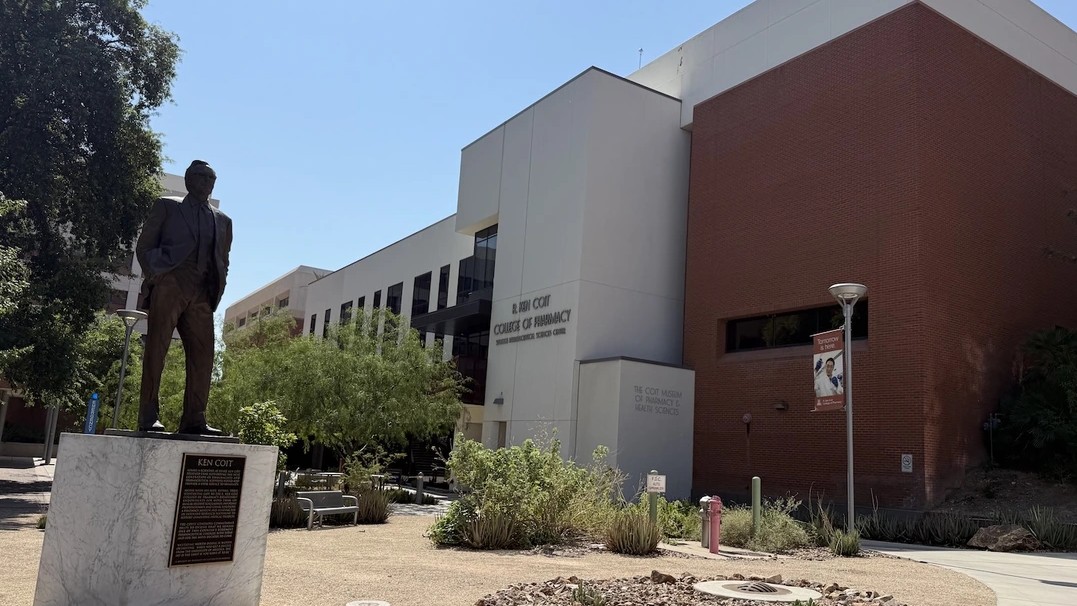 Image of the R. Ken Coit College of Pharmacy building on the U of A campus with a statue of a man in the foreground.