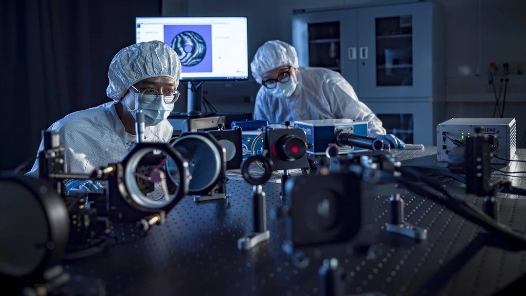 Postdoctoral researcher Hyukmo Kang (left) and Optical Sciences graduate student Solvay Blomquist, both in white protective gear, align space telescope optics in the U of A's Applied Research building.