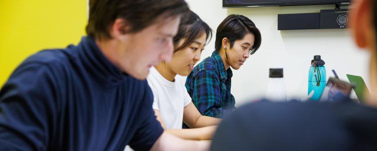 Photo of two male students and a female student doing schoolwork and looking at computer screens 