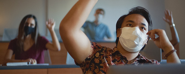 Image of students in facemasks in a classroom with raised hands