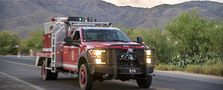 Photo of a fire truck heading down a road with mountains and smoke in the distance