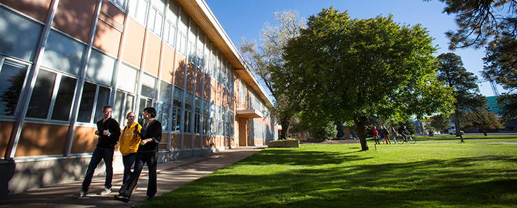 Photo of three students walking on NAU campus next to a building with trees in the background. 