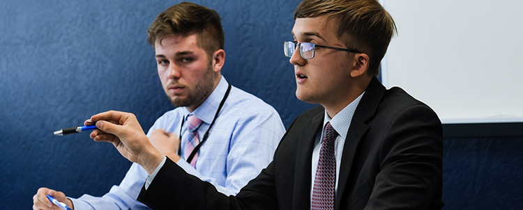 Two male students participate in the Regents' Cup with one of the students speaking and gesturing with his hand. 