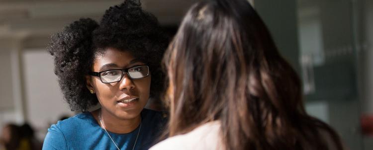 Woman with glasses conversing with another woman with her back to the camera.