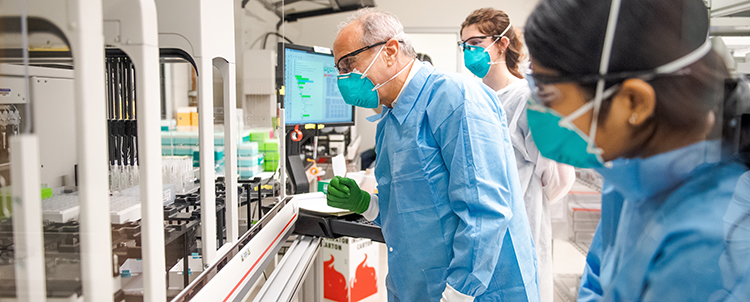 Photo three researchers in masks, safety glasses and gowns in a lab 