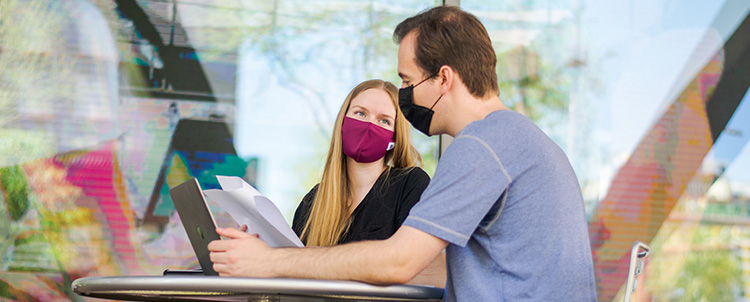 Two students in front of laptop studying with facemasks on.  